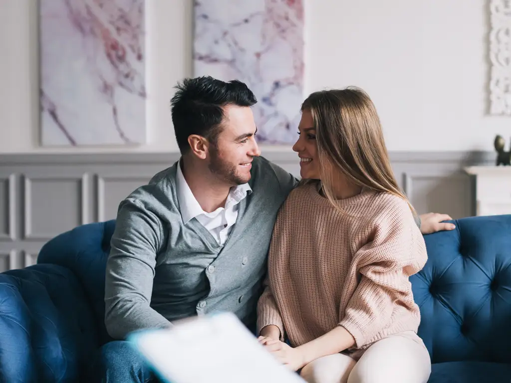 Smiling couple sitting close together on a couch, looking at each other with warmth.