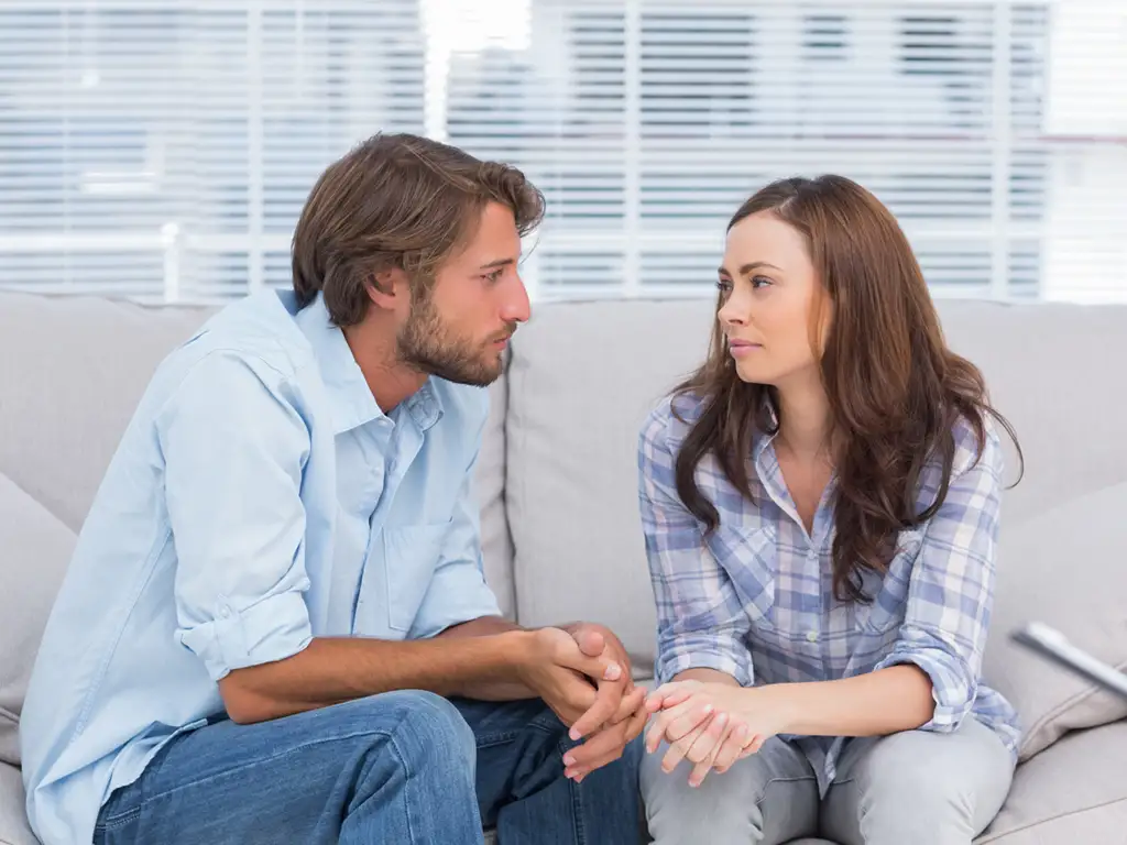 Couple seated together on a couch making eye contact during a counseling session.